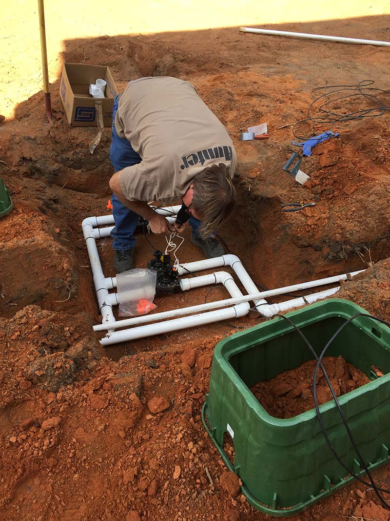 Irrigation install working in the dirt to connect the sprinkler pipes